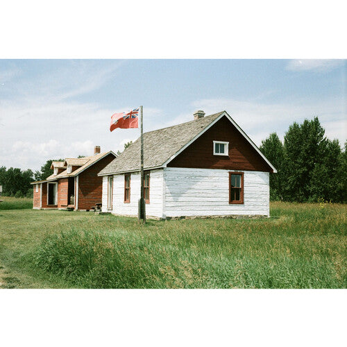 Two older square shaped wood homes, one red and one white and red with a red flag outside and green grasses and trees surrounding