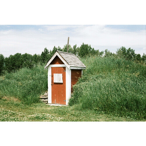 White and red small shed with green trees and bushes around it and a blue ocean in the distance