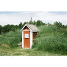 White and red small shed with green trees and bushes around it and a blue ocean in the distance