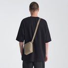 Person wearing a black t-shirt with a beige crossbody bag on a white background